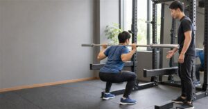 セーフティーバーを設定したスクワットラックで20kgのバーを使いフォームを確認する初心者